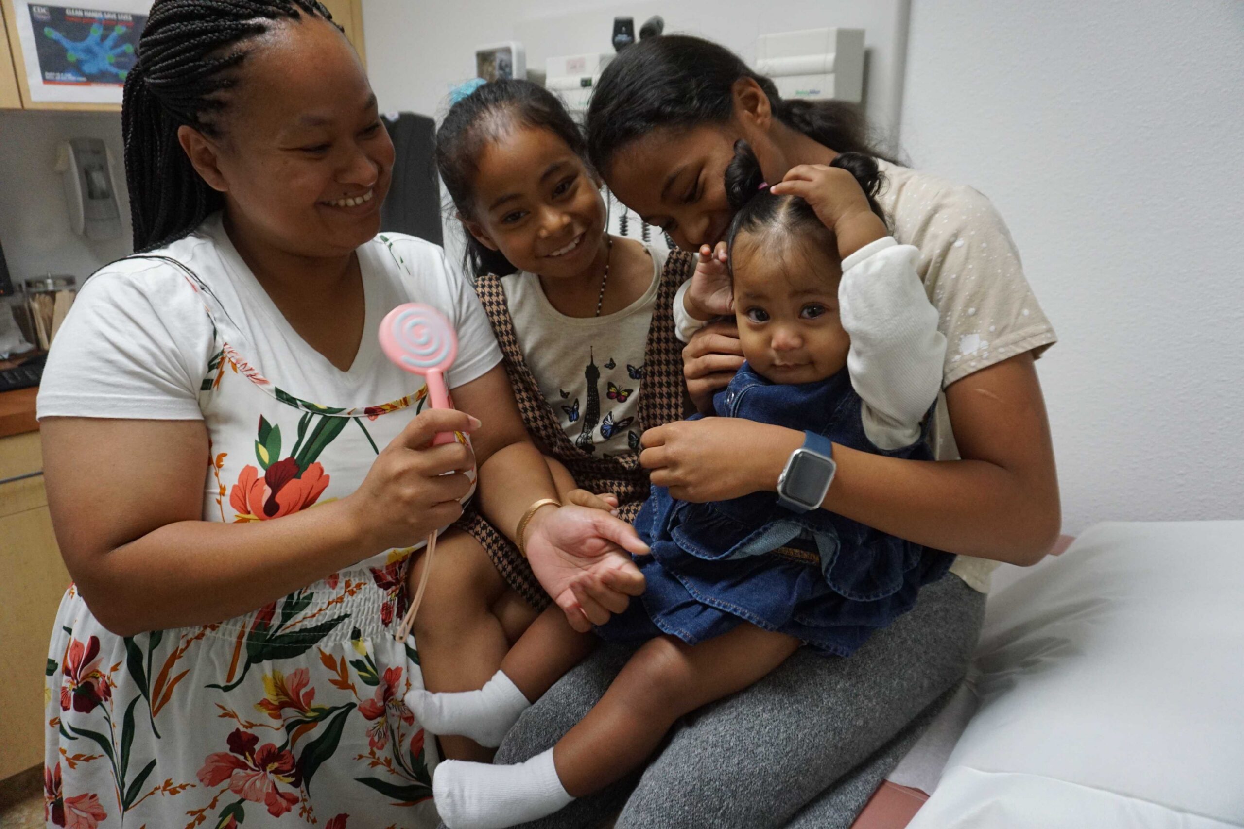 Group seated in a medical exam room with a child positioned on the examination table