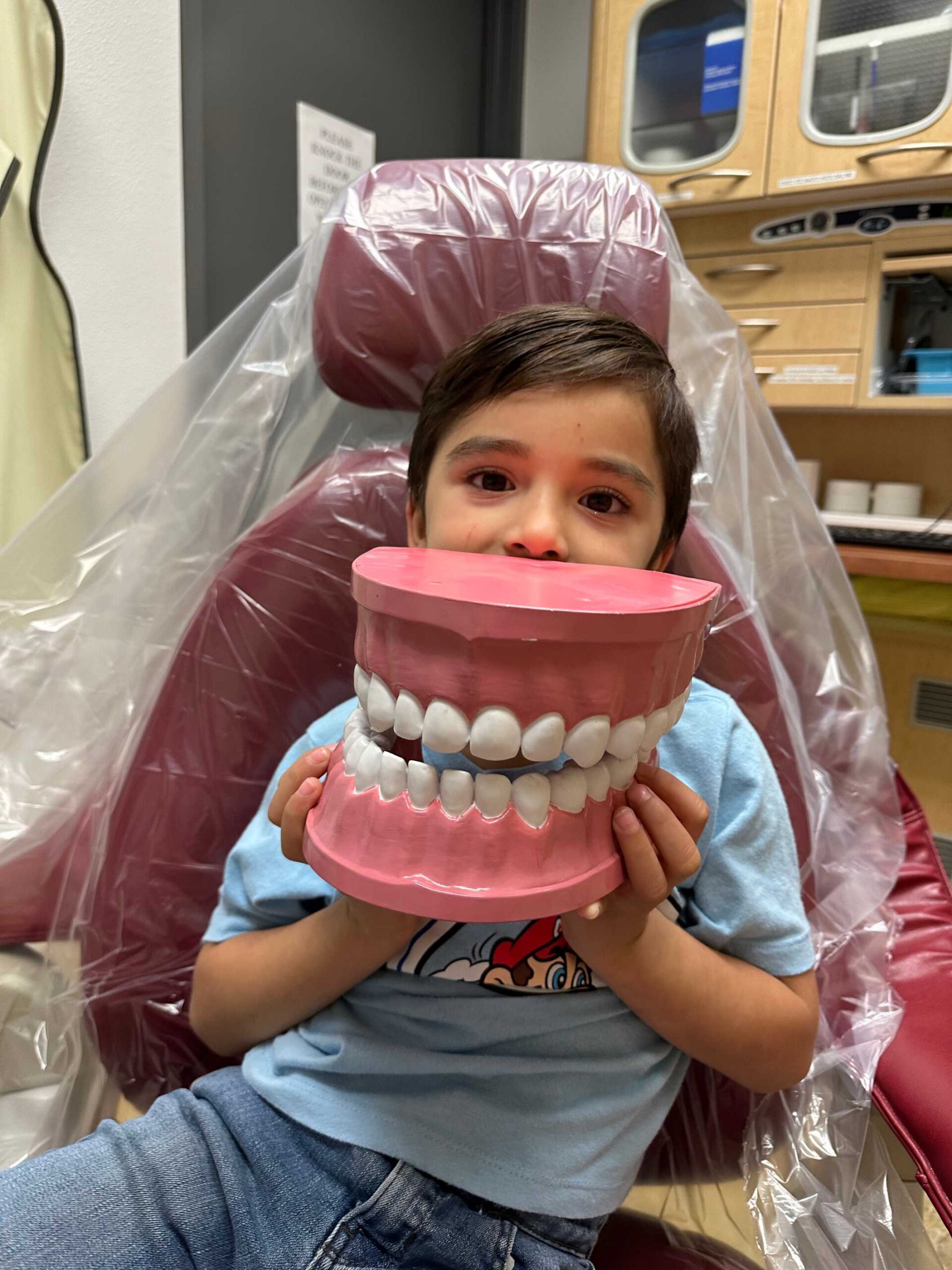 Child seated in a clinic holding a large dental model during a health education visit
